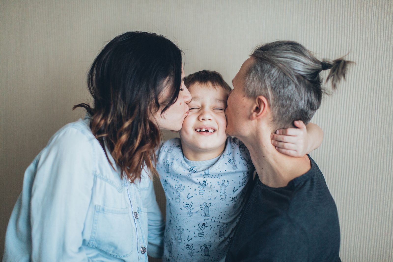 A mother and father lovingly kissing their smiling son on the cheeks in soft natural light