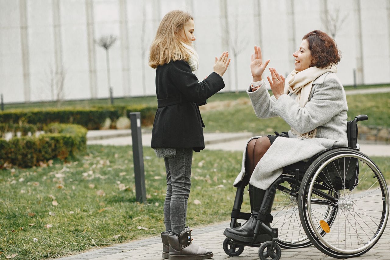 A girl playing a clapping game with a smiling woman in a wheelchair