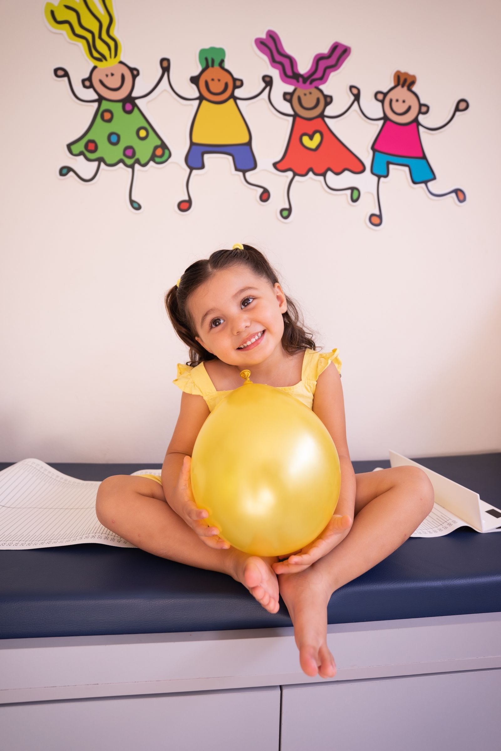 A happy little girl smiling in a bright children's clinic, holding a golden balloon