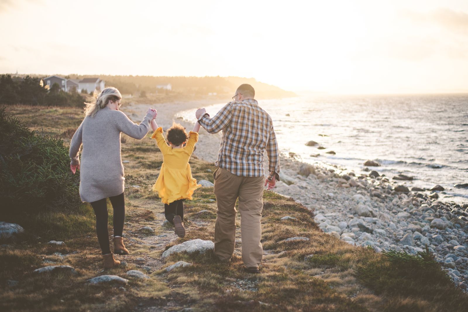 Parents holding their daughter's hands and swinging her joyfully as they walk into the warm golden sunrise by the sea